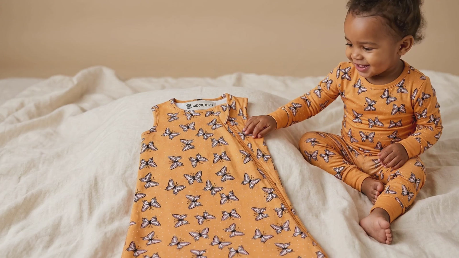 Toddler sitting on a bed in matching mustard butterfly-print pajamas, next to a matching sleep sack