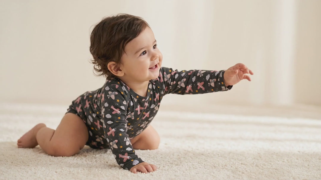 Baby crawling on a rug wearing a charcoal bamboo bodysuit with an airplane and cloud print
